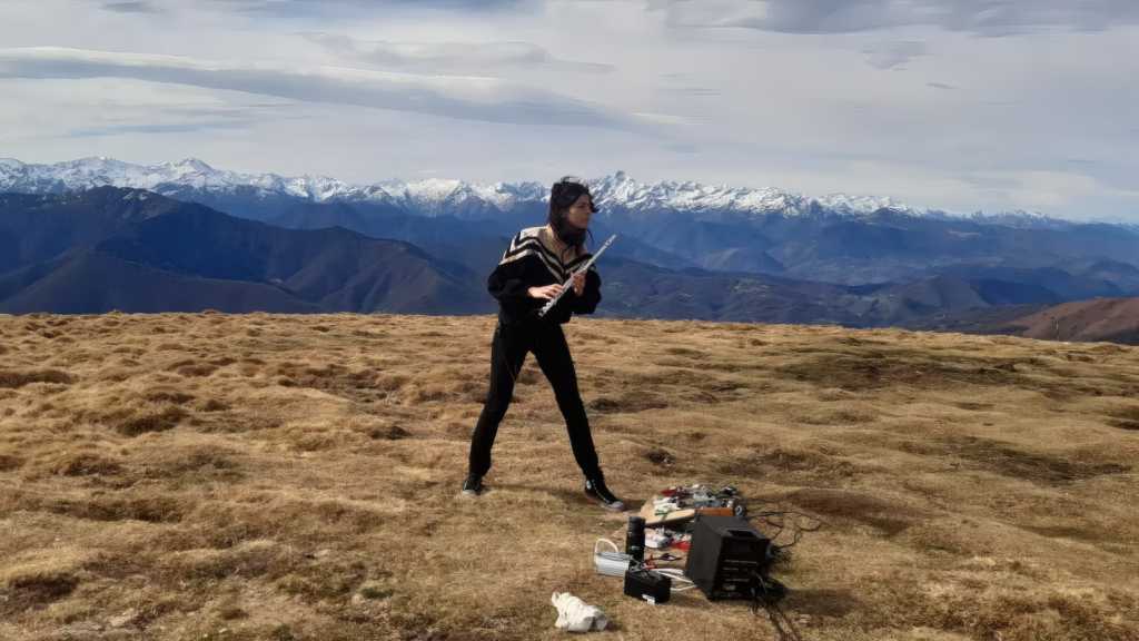 Musikerin Delphine Joussein steht auf einem Bergplateau und spielt Querflöte